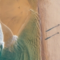 Top-down view of couple walking along sandy beach washed by Atlantic Ocean waves in Portugal casting long shadows in low sunrise light. Shot during the Camino Portuguese