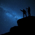 Hikers on rock enjoying view of night sky