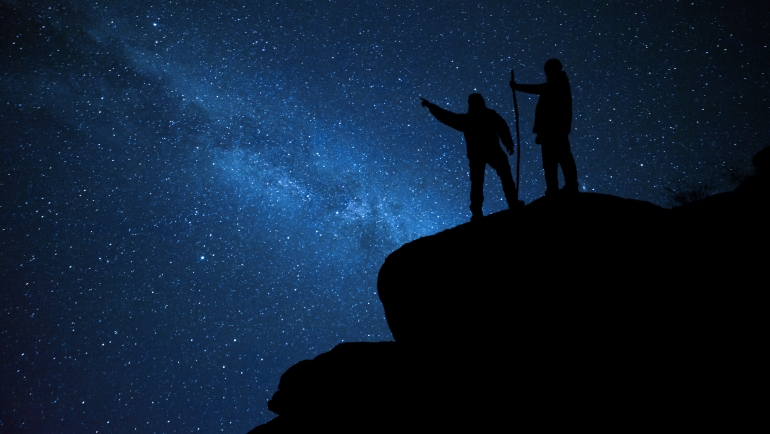 Hikers on rock enjoying view of night sky
