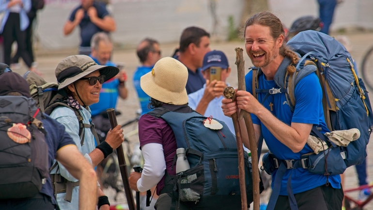 smiling pilgrims holding walking sticks celebrate their achievement after completing the camino de santiago in santiago de compostela