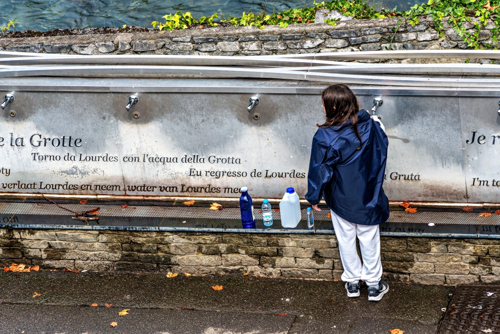 Pilgrims to the Sanctuary of Lourdes in France, Europe filling bottles with holy water