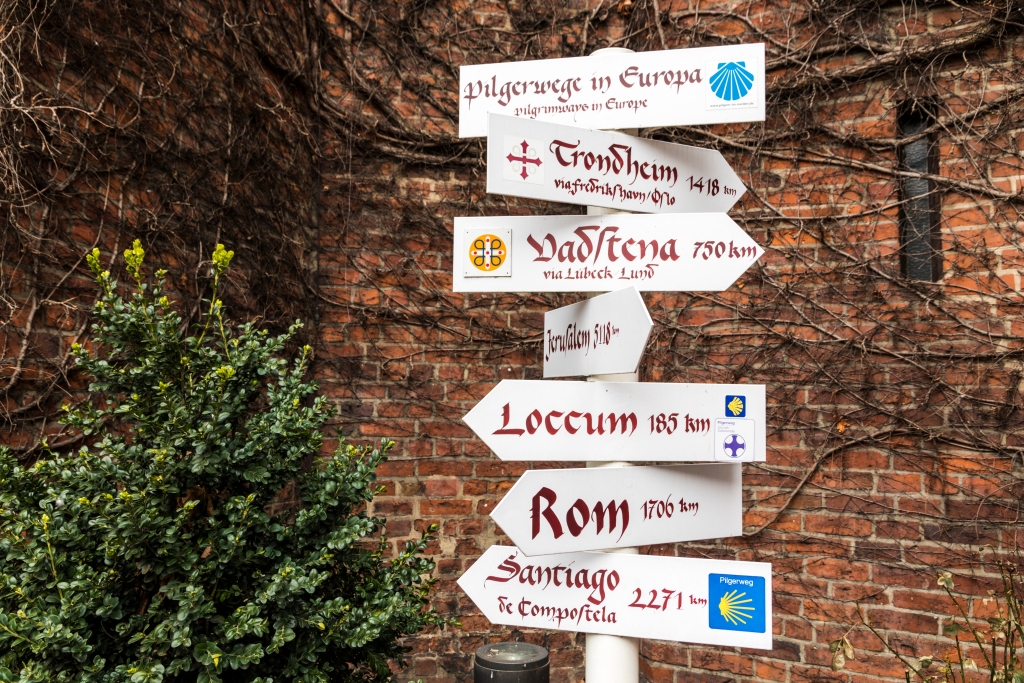HAMBURG, GERMANY - March 27, 2018: Directions sign post with European pilgrimage routes as the Camino de Santiago (Way of St James) and Pilegrimsleden (St. Olav's Way), St. James' Church