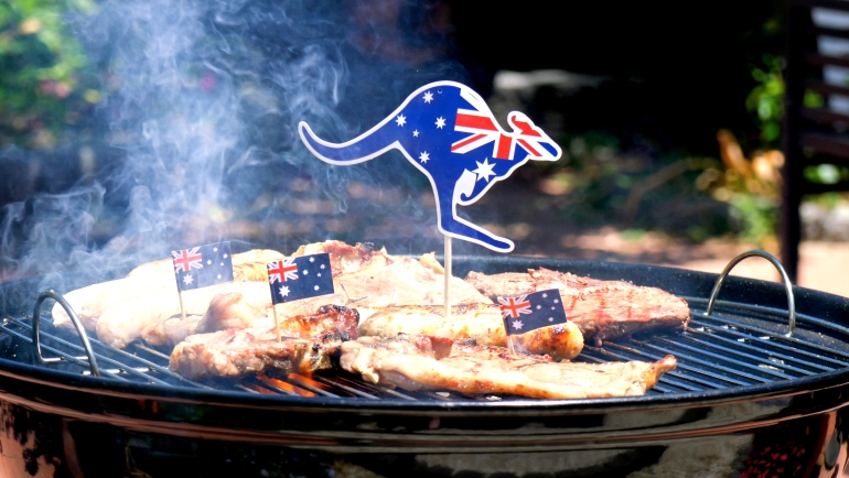 Icónica barbacoa australiana cerca de muchas costillas de cocina, salchichas y bistec, al aire libre en el jardín.
