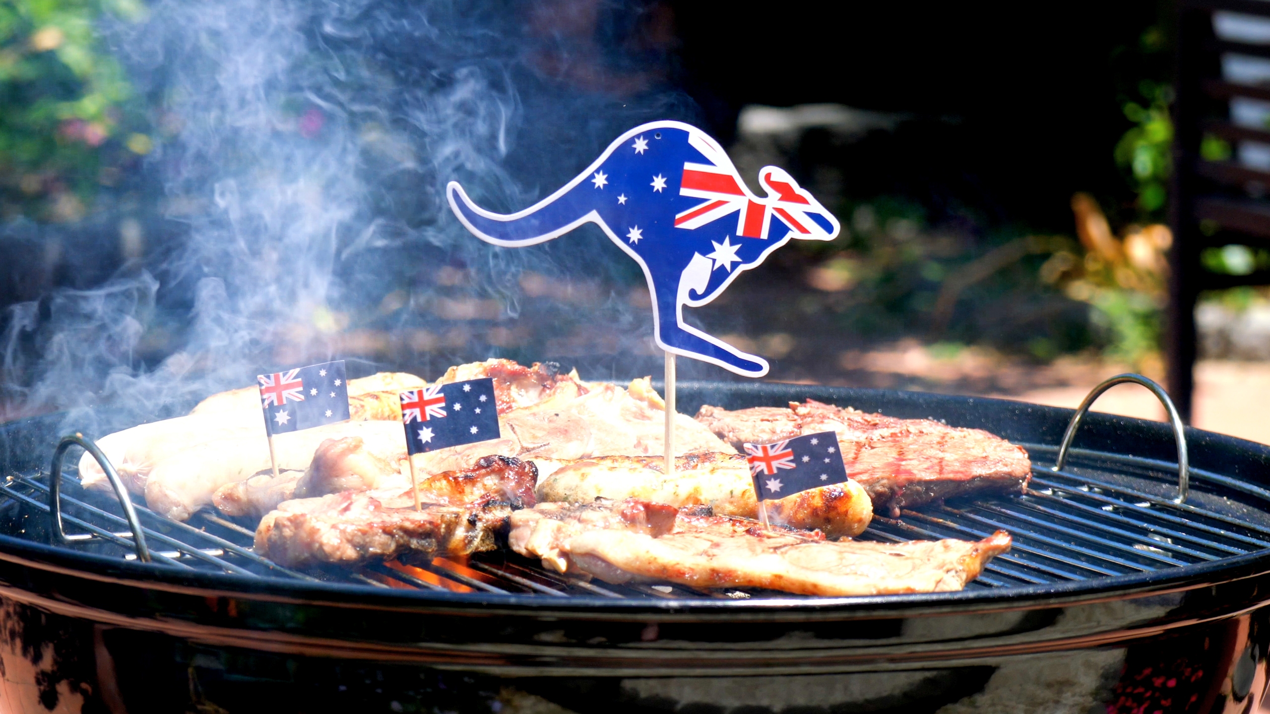 Icónica barbacoa australiana cerca de muchas costillas de cocina, salchichas y bistec, al aire libre en el jardín.