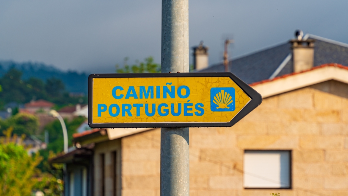 A directional sign on the Camino de Santiago with scallop shell and yellow arrow symbols in Tui, Spain