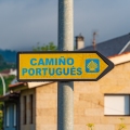 A directional sign on the Camino de Santiago with scallop shell and yellow arrow symbols in Tui, Spain