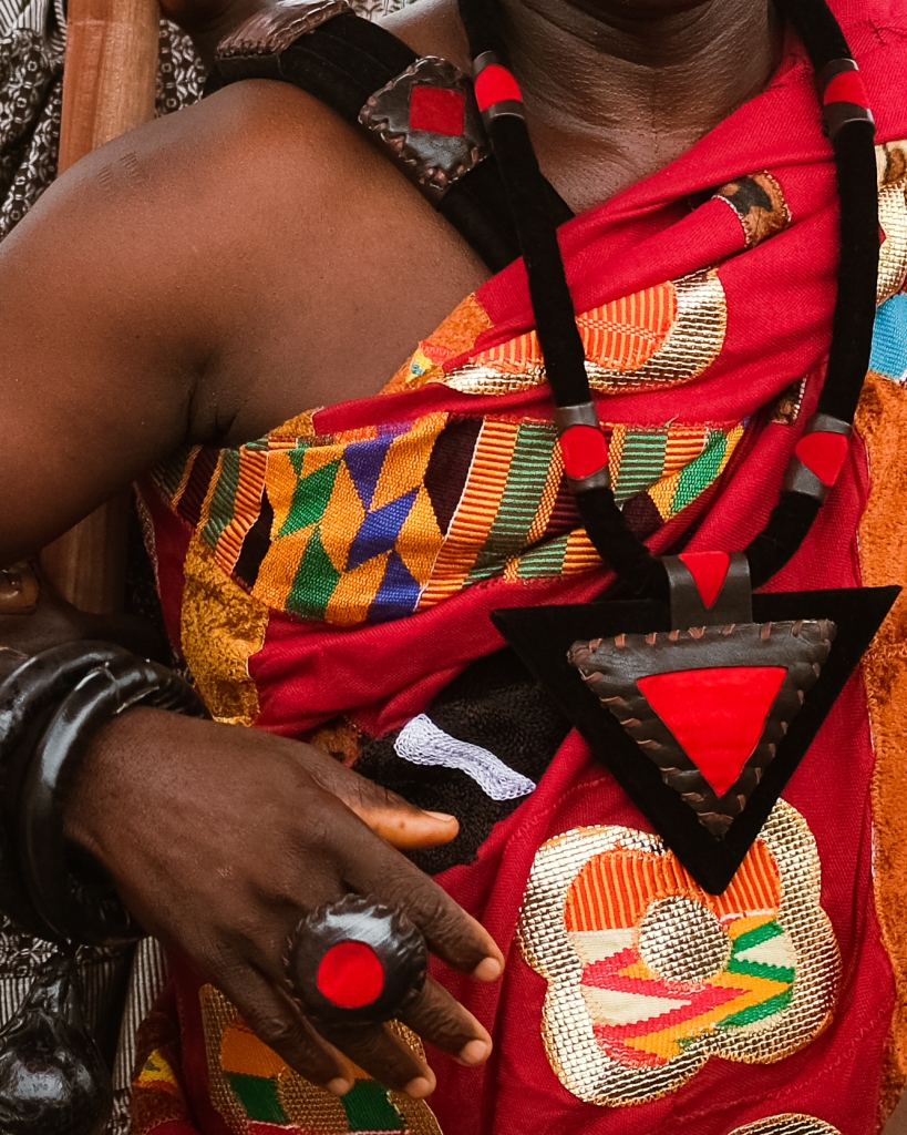 Close-up detail of a chief's regalia showing hand-woven kente cloth, leather ornaments with red accents, and a carved ring, during the Fetu Afahye Festival, Cape Coast, Ghana