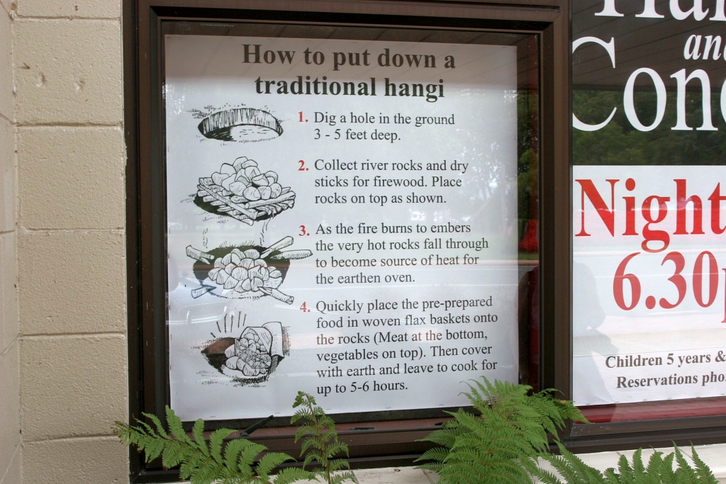 Rotorua, New Zealand. A white sign describes how to prepare a traditional *hāngī*. It includes four steps with illustrations.