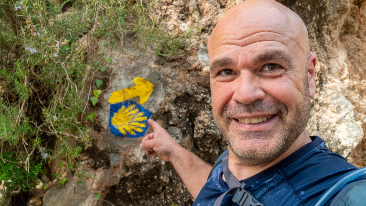 A pilgrim takes a selfie next to the symbols of the Camino de Santiago: the scallop shell and an arrow.